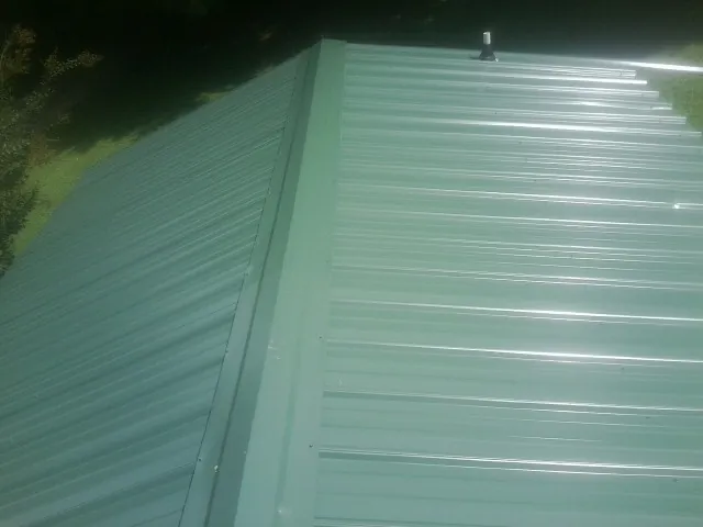 New green metal panels meeting at the ridge of a roof — Flat Roof Repair work by our crew in Rice