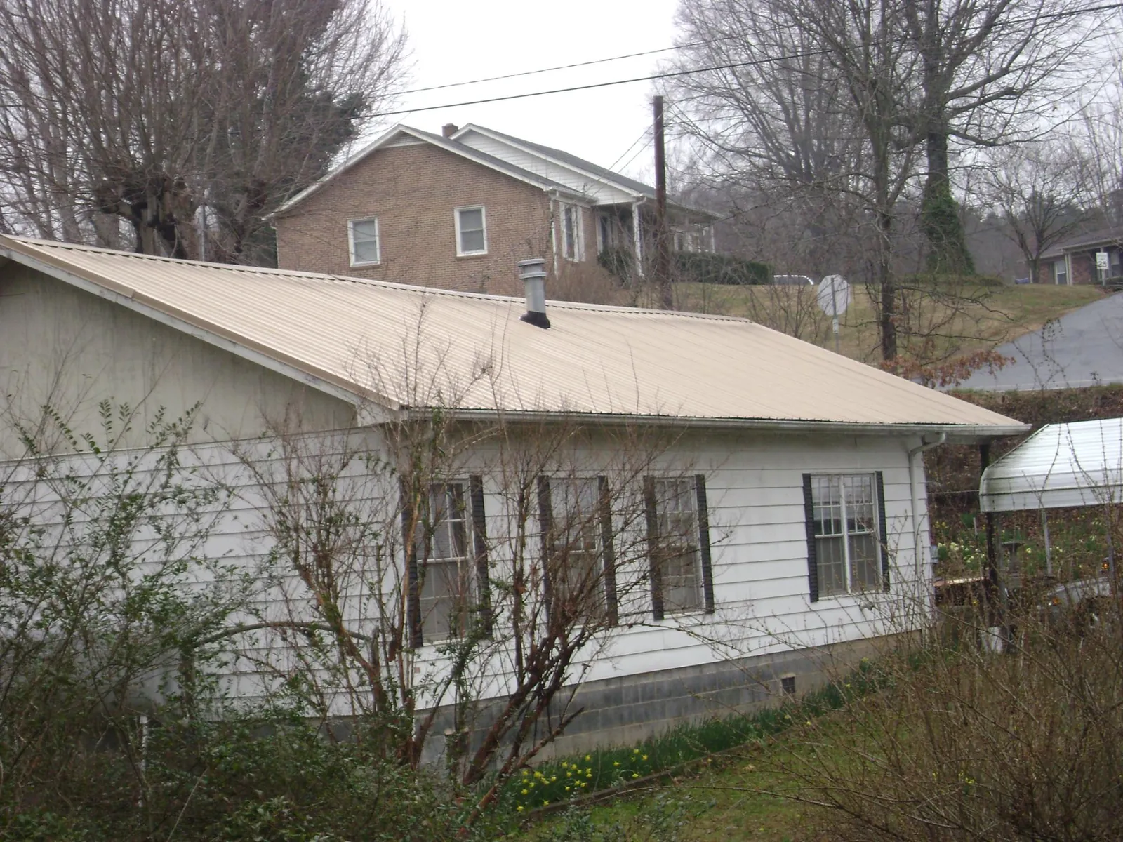 Tan metal roof on a white sided house set into a hillside — Commercial Roofing by Roofing Brothers in Rice
