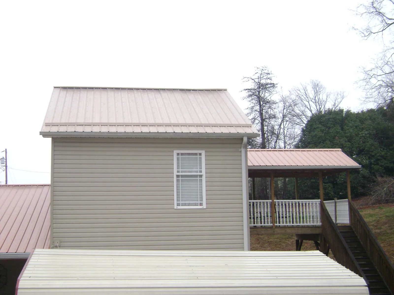Tan metal roofs on a two story addition and attached porch, from a Roof Replacement job in Rice